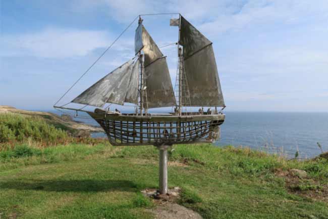 Sculpture of a sailing boat on a grass headland overlooking the sea